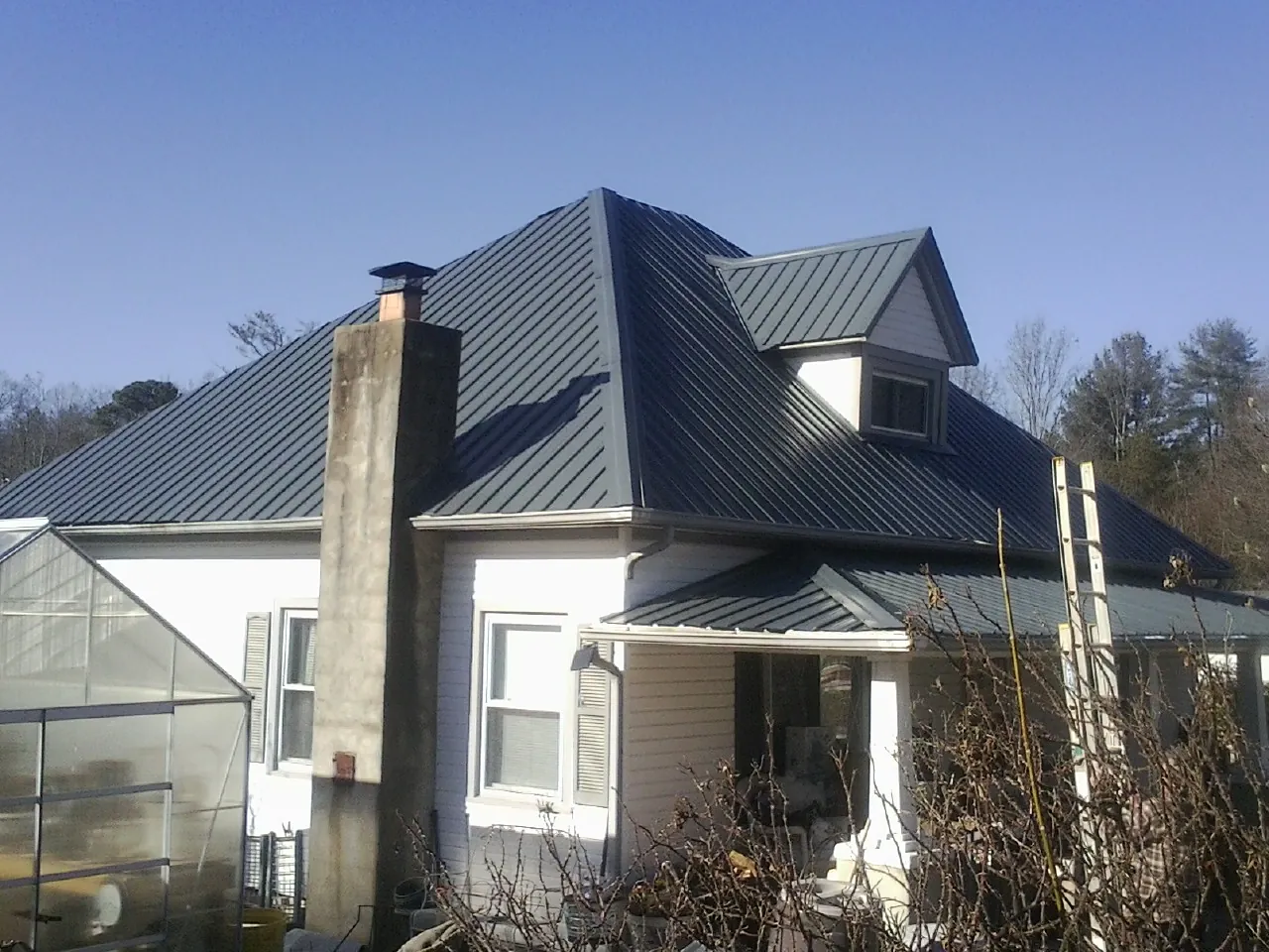 Dark blue standing seam metal roof on a white farmhouse with dormer — Slate & Tile Roof Repair by Roofing Brothers in Alvin