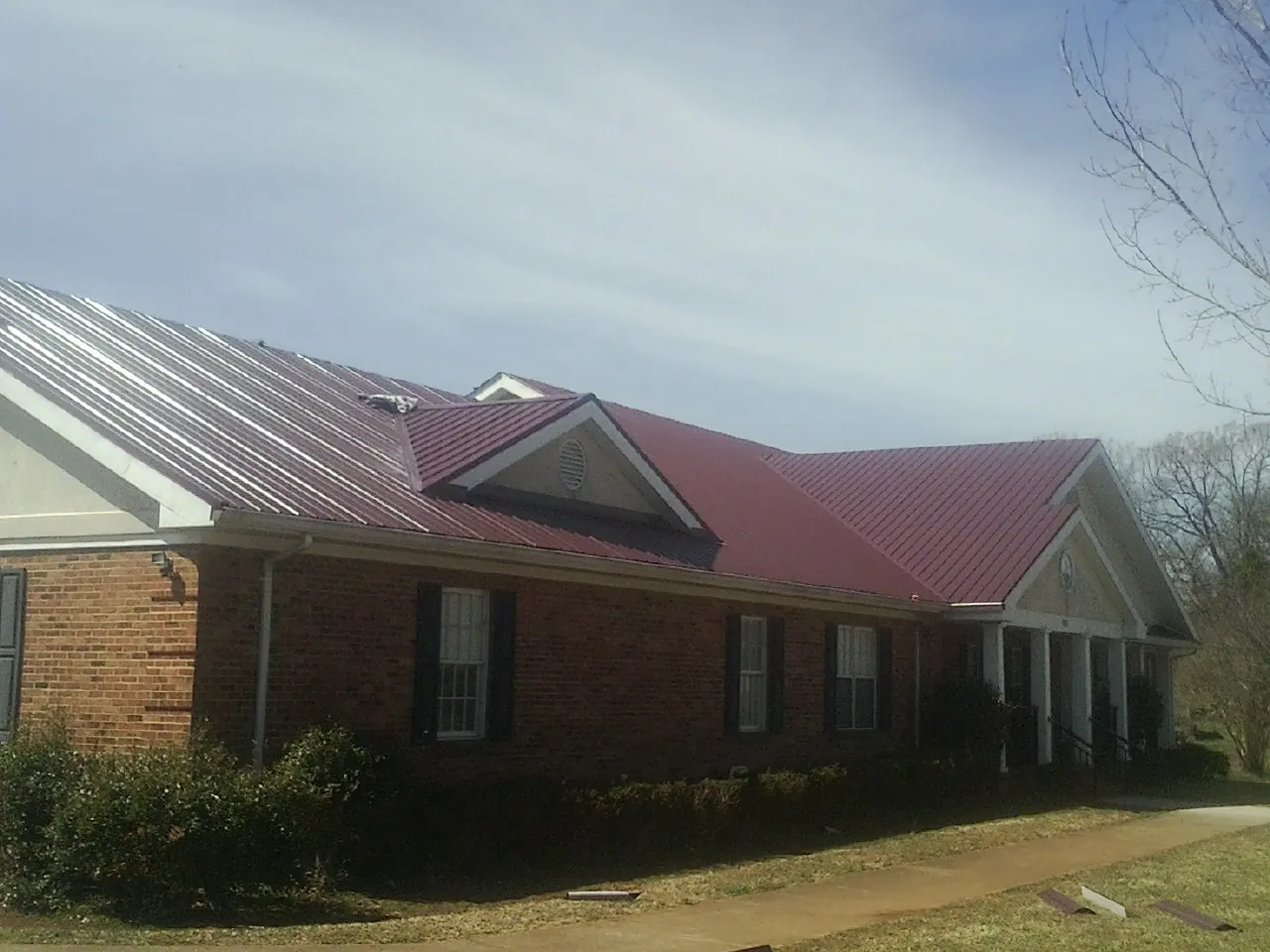 Red metal roof with gabled entries on a long brick building, from a Hail Damage Roof Repair job in Alvin