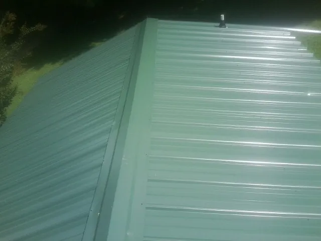 New green metal panels meeting at the ridge of a roof — Flat Roof Repair work by our crew in Alvin