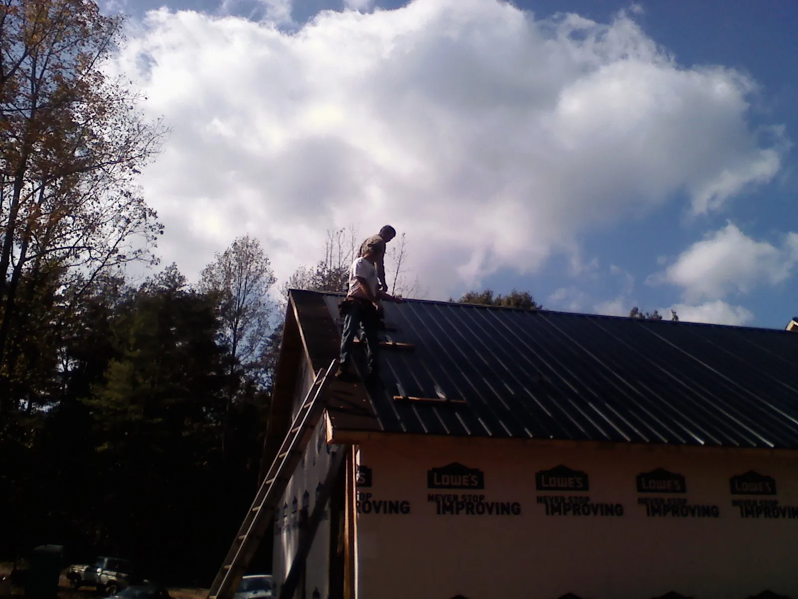 Roofer fastening dark metal panels high against a cloudy sky, from a Roof Inspection job in Alvin