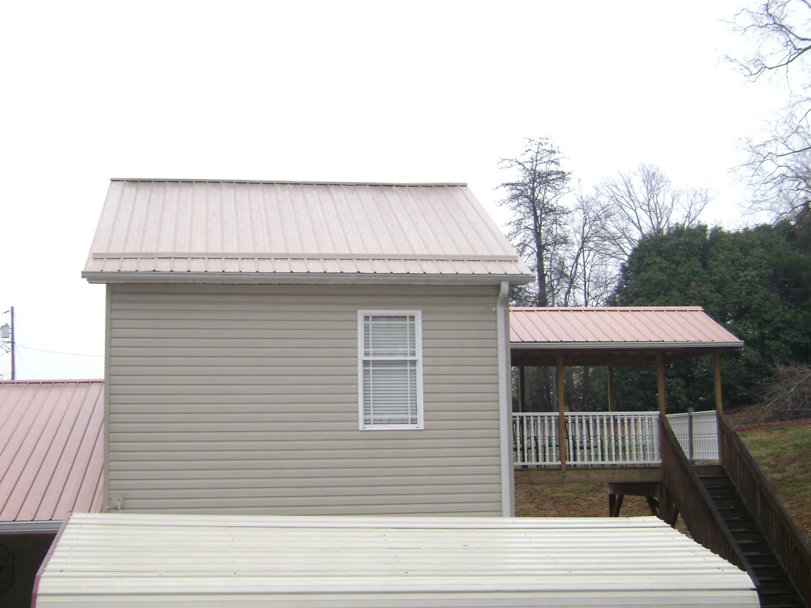 Tan metal roofs on a two story addition and attached porch, from a Roof Replacement job in Alvin